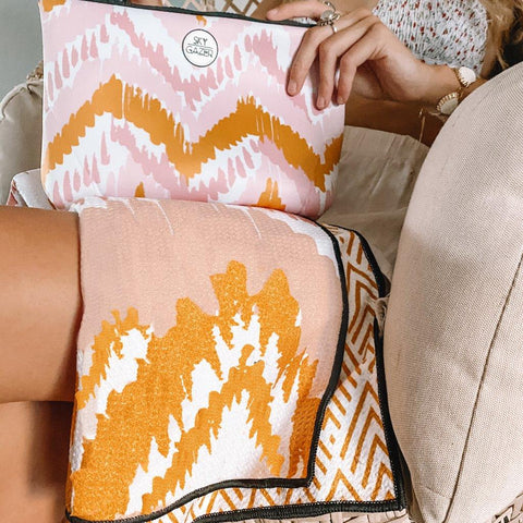 Girl holding Sky Gazer sand free towel on her knee with the zipped wet bag. Design pink, yellow and white zig zag. The design is called The Airlie.