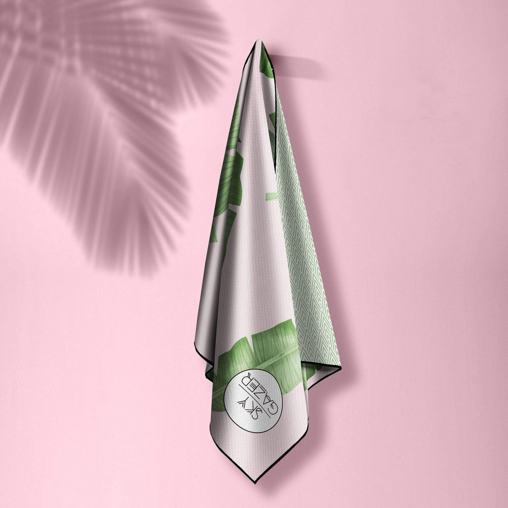 the Balmoral Sky Gazer sand free beach towel is hanging up on a wall with a pink background