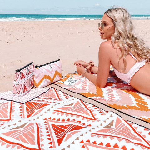 pretty girl laying on airlie beach with 2 Sky Gazer sand free towels and matching wet bags. The designs are called The Lennox and The Airlie.