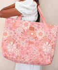Person holding a pink floral-patterned tote bag against a neutral background