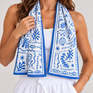 A woman wearing a white tank top and white drawstring shorts with a blue and white patterned cooling towel draped around her neck, photographed against a light neutral background.