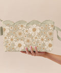 Hand holding a floral-patterned scalloped wet bag style pouch against a beige background