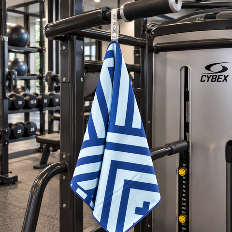 A blue and white patterned gym towel hangs from a pull-up bar on a Cybex strength training machine inside a gym.