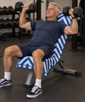 A man in a gym wearing a navy blue t-shirt and matching shorts, sitting on a blue and white striped weight bench while lifting hex dumbbells.