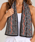 A woman wearing a brown-colored cooling towel scarf with a black and white chain-link pattern, styled over a white tank top and white drawstring pants.