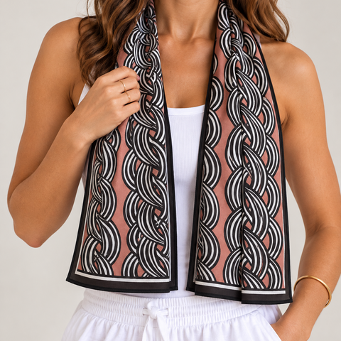 A woman wearing a brown-colored cooling towel scarf with a black and white chain-link pattern, styled over a white tank top and white drawstring pants.