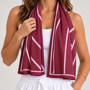 A woman wearing a burgundy mesh cooling scarf with white geometric stripes, draped around her neck over a white tank top and white drawstring shorts.