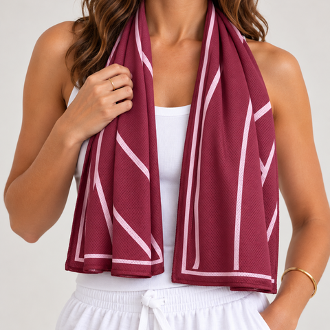 A woman wearing a burgundy mesh cooling scarf with white geometric stripes, draped around her neck over a white tank top and white drawstring shorts.