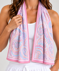 A woman wearing a white tank top and white drawstring shorts, with a pink indigenous cooling towel draped around her neck like a scarf. 