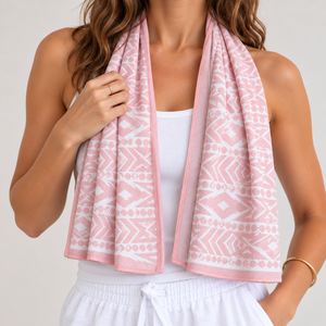A woman wearing a pink and white patterned cooling towel draped around her neck, paired with a white tank top and white drawstring shorts, against a light gray studio background.