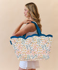 Woman holding a scallop floral tote beach bag with blue handles against a beige background