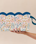 scalloped and Floral-patterned wet bag with blue handles held by a hand on a beige background