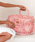 Person holding a pink floral patterned cooler bag on a beige background