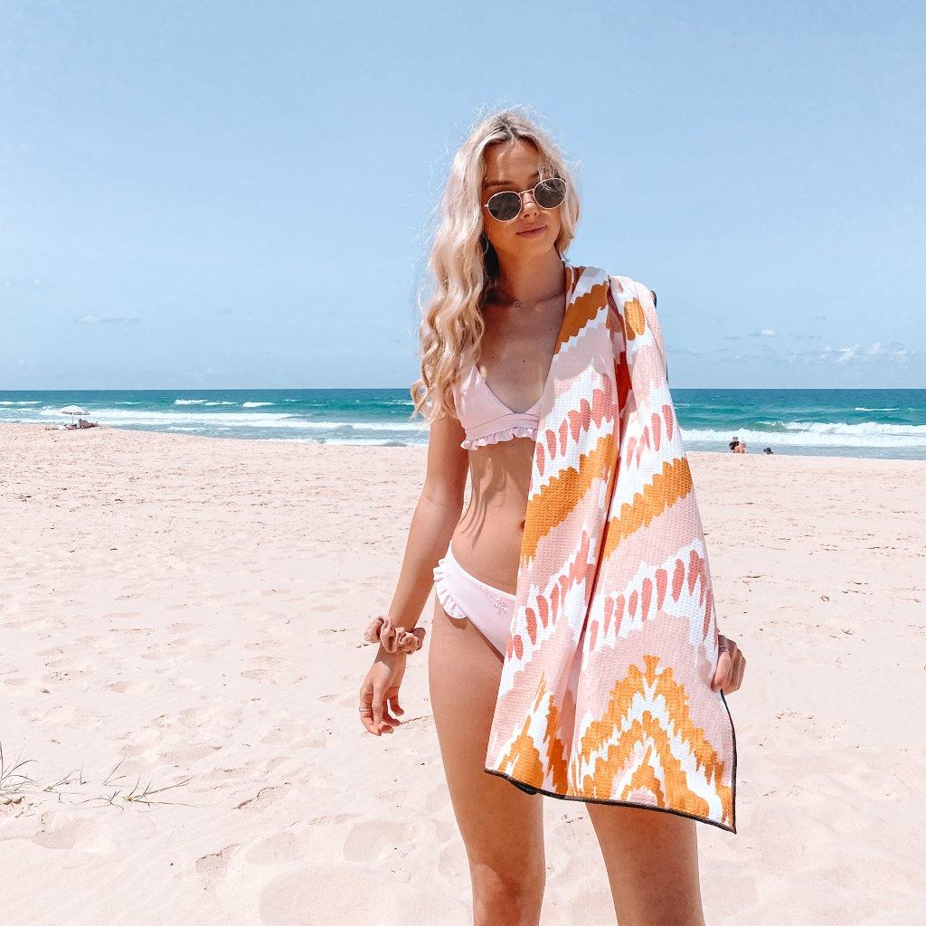 pretty girl with blonde hair on Airlie beach with Sky Gazer's quick dry towel in pink and yellow zig zag called The Airlie. 